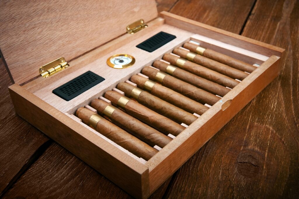 Cigars in a wooden box on a wooden table alongside a hygrometer.