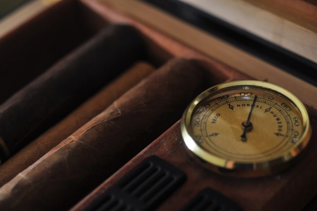 Cigars and a compass in a wooden box, featuring an analog hygrometer.
