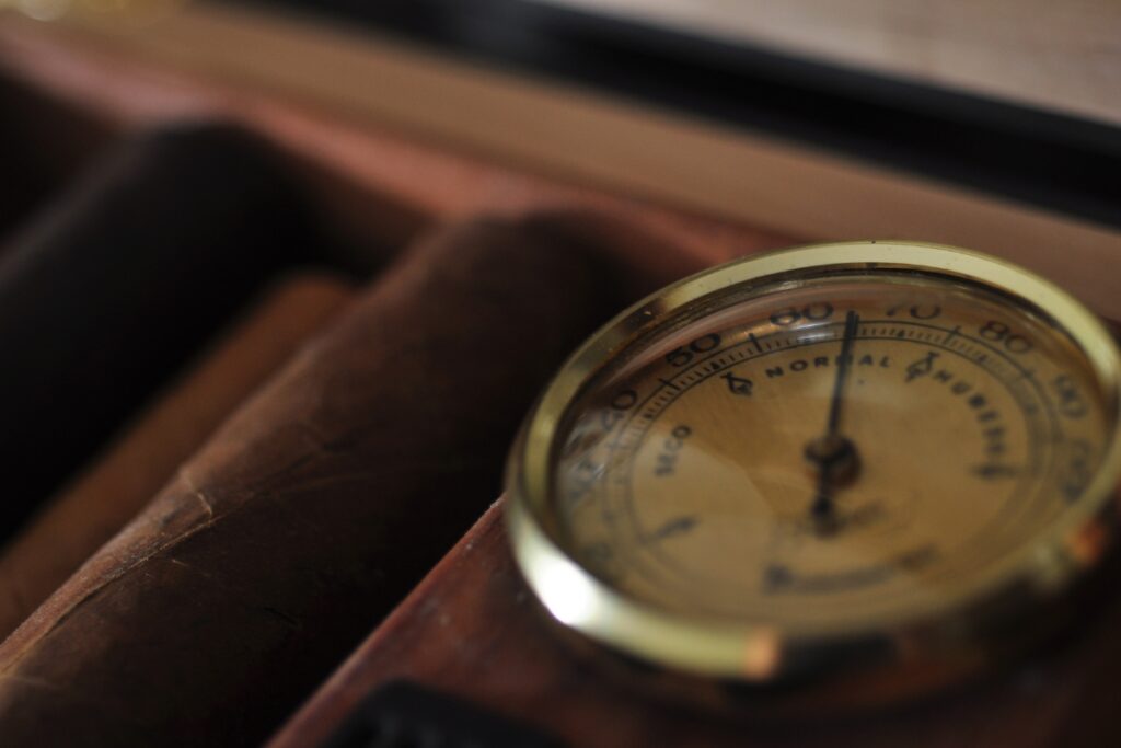 An analog thermometer sits on top of a cigar box.