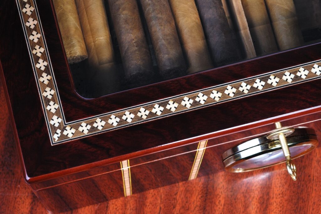 An analog hygrometer is placed inside a cigar humidor, which is set on a wooden table.