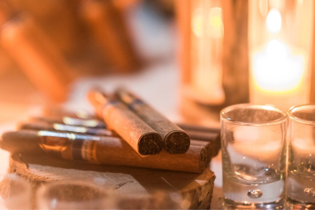 Authentic smoke swirls around a Puro cigar and a pair of glasses on a wooden table, hinting at the secrets that lie within.