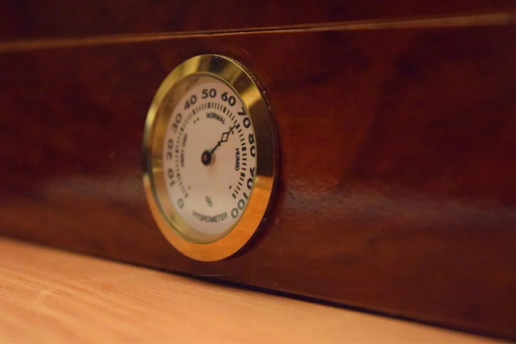 A close up of a clock on a wooden table, reminding you about the importance of regular humidor maintenance.