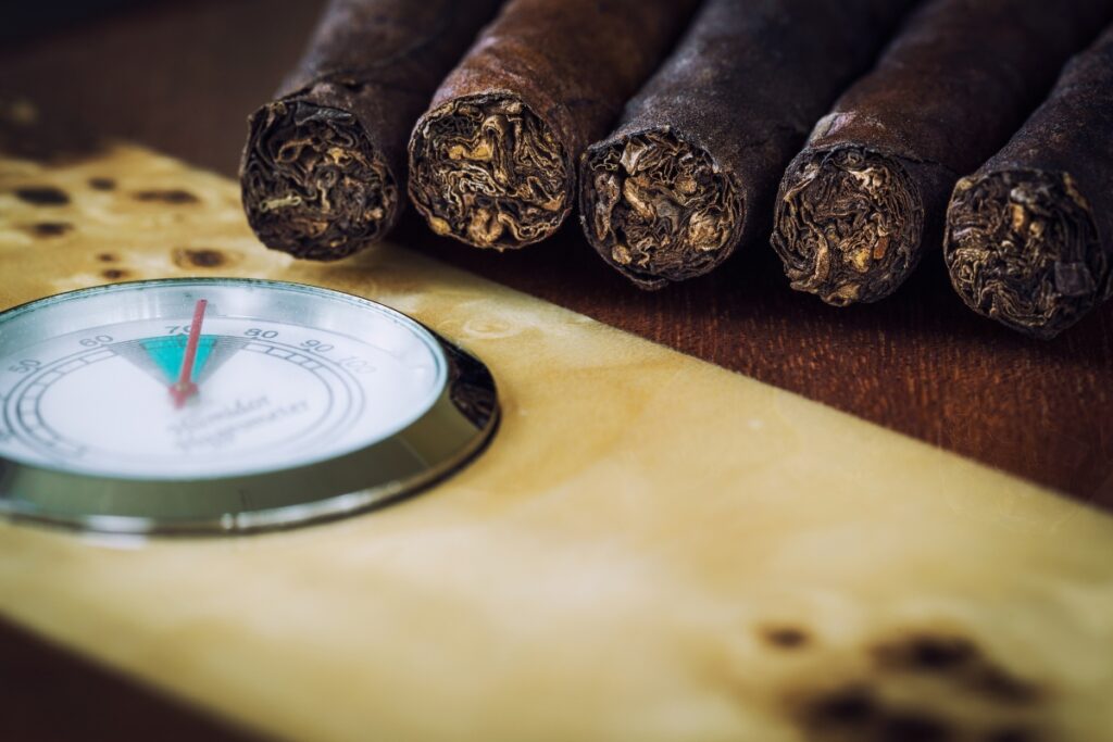A wooden table hosts a display of cigars alongside a thermometer, ensuring optimal humidor maintenance.