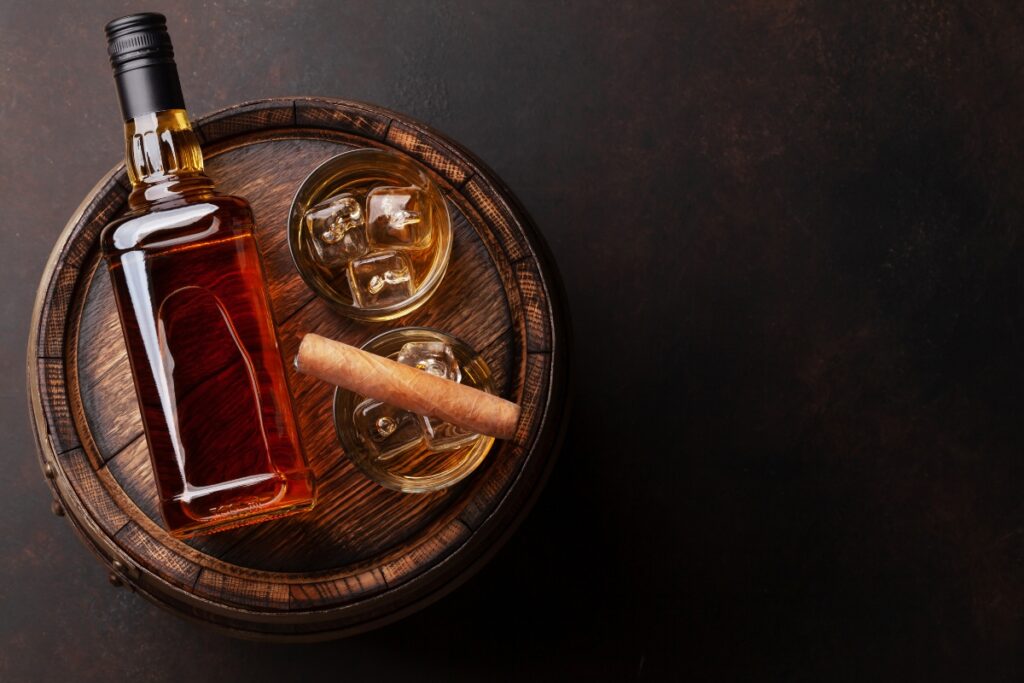 A bottle of whiskey and a cigar, perfect for pairings, on a wooden barrel.