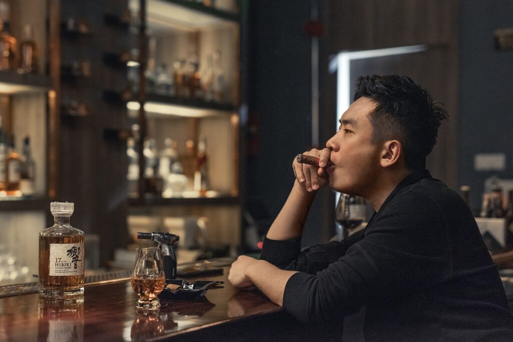 A man sitting at a bar looking at a bottle of whiskey, contemplating cigar and whiskey pairings.