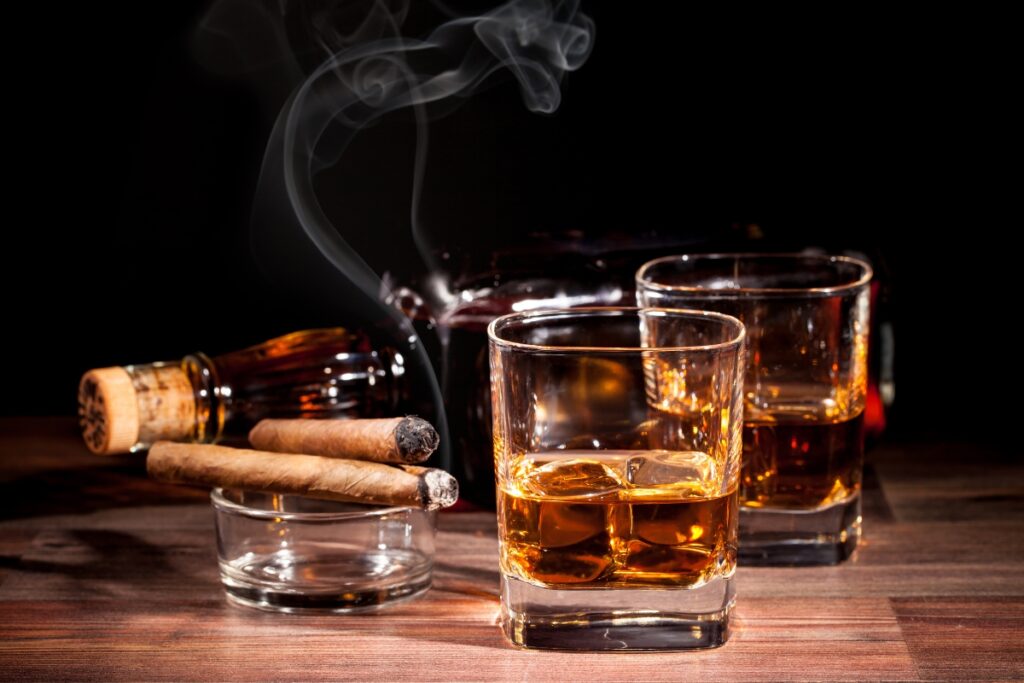 A glass of whiskey and cigar pairings on a wooden table.