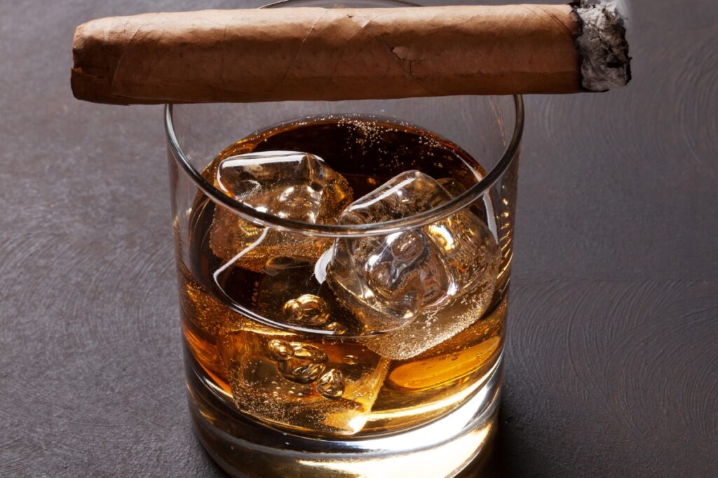 A glass of whiskey with ice and a cigar arranged for specific cigar and whiskey pairings.