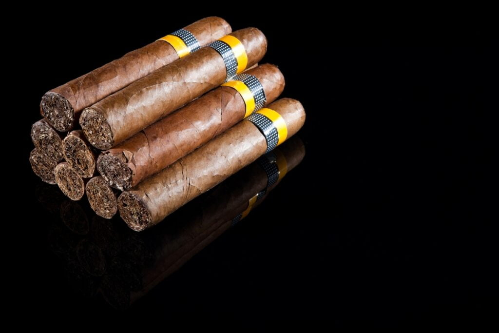 A stack of hand-rolled tasting cigars with yellow bands on a reflective black surface.