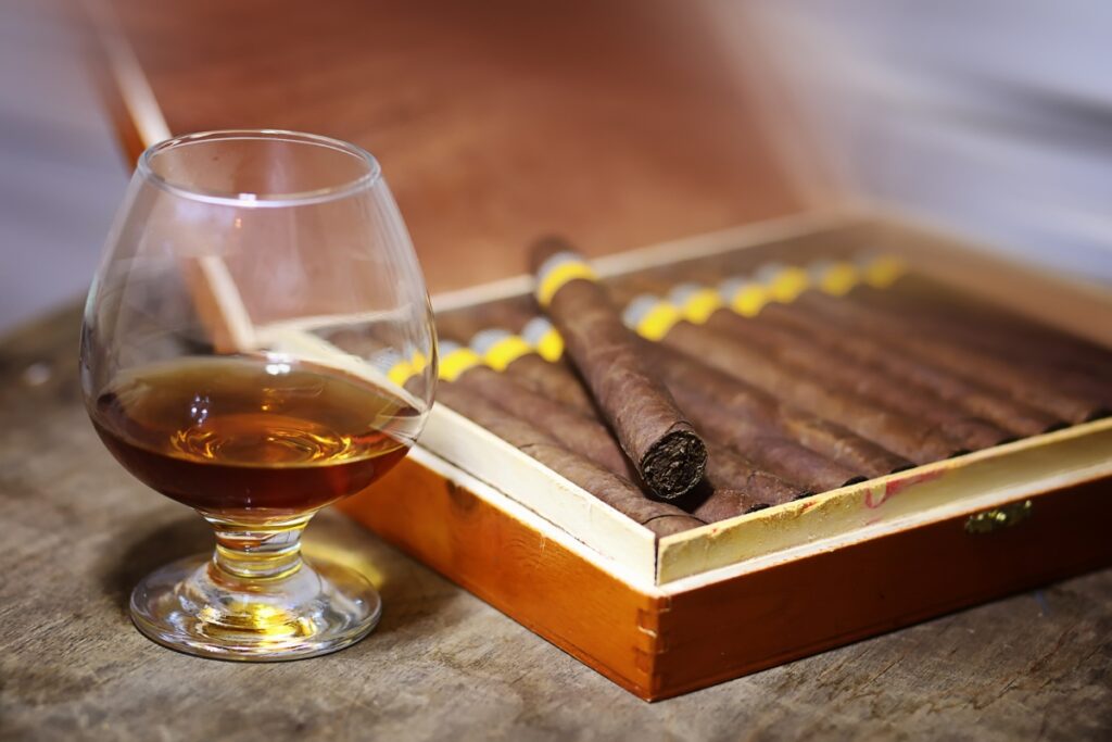 A glass of cognac beside an open box of tasting cigars.