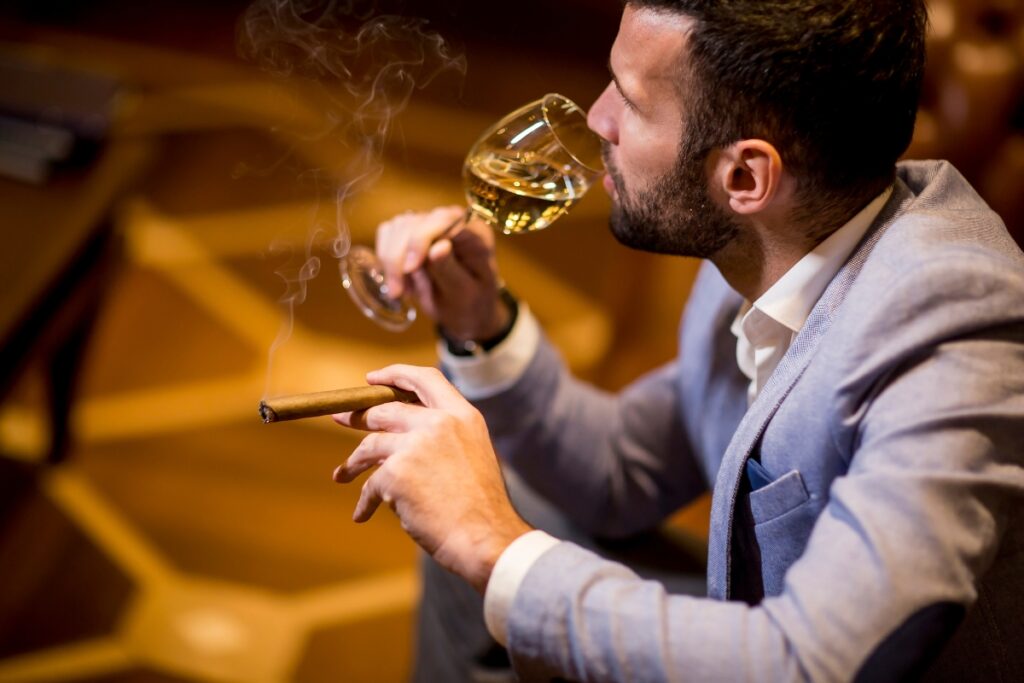 Man in a suit adhering to cigar etiquette while enjoying a glass of whiskey.