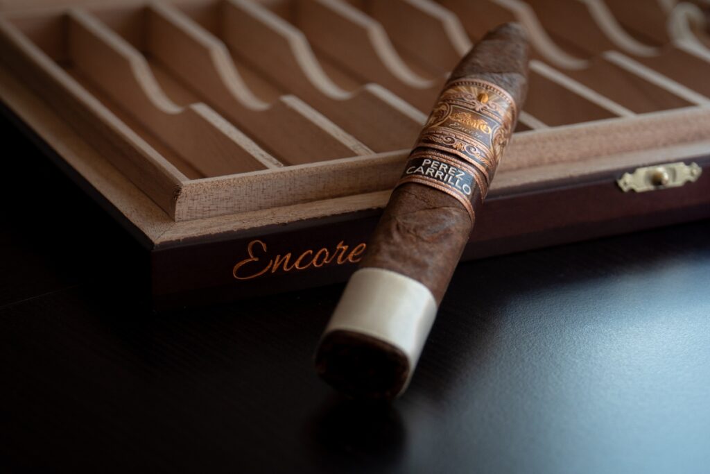 A close-up of a cigar labeled "perez carrillo encore" resting on an open wooden cigar box, embodying current cigar trends.