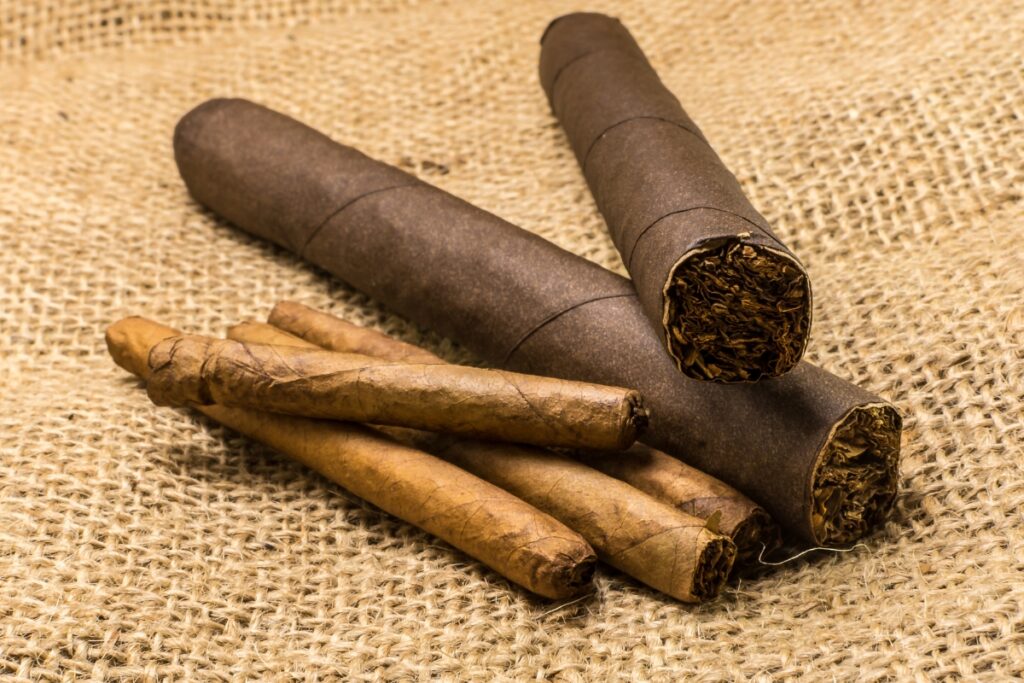 Two large, dark cigars following cigar trends overlap three smaller, light cigars on a textured burlap surface.