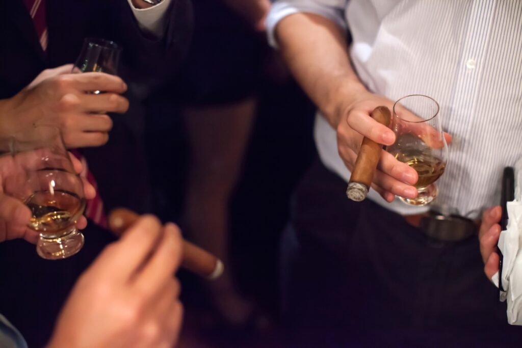 Close-up of hands holding glasses of whiskey and a cigar at cigar events.