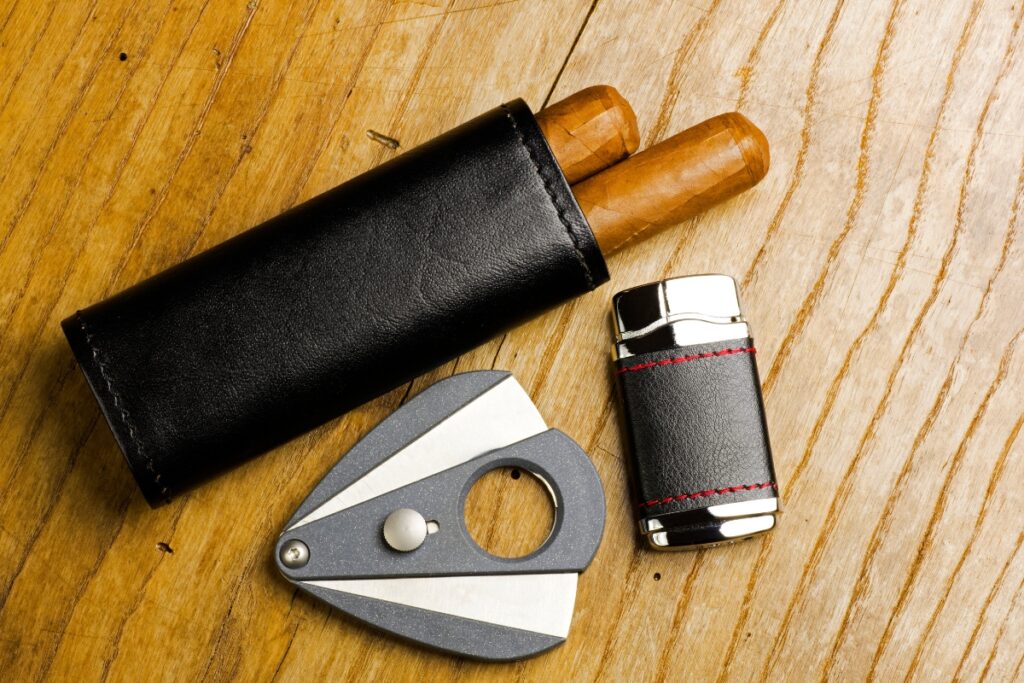 Luxury cigar accessories including a cigar holder with two cigars, a finely crafted cigar cutter, and a sleek lighter elegantly arranged on a wooden surface.