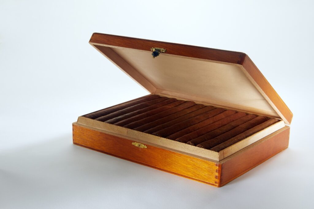 A wooden humidor with an open lid reveals the pride of cigar collecting, showcasing multiple rows of fine cigars inside.