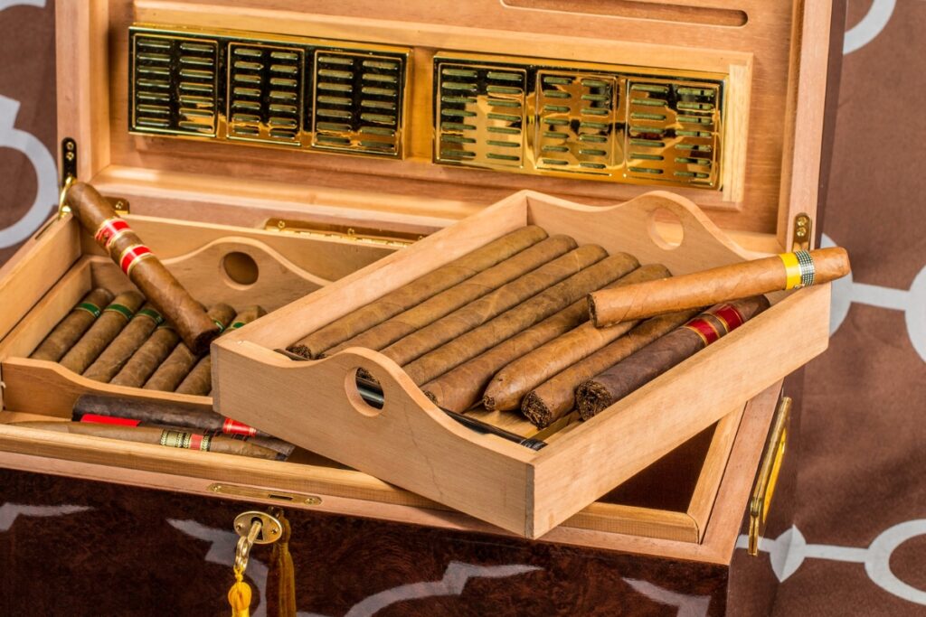 A wooden humidor filled with cigars, featuring a tray inside holding additional cigars, all arranged neatly—perfect for those who appreciate quality and also need travel humidors on the go.