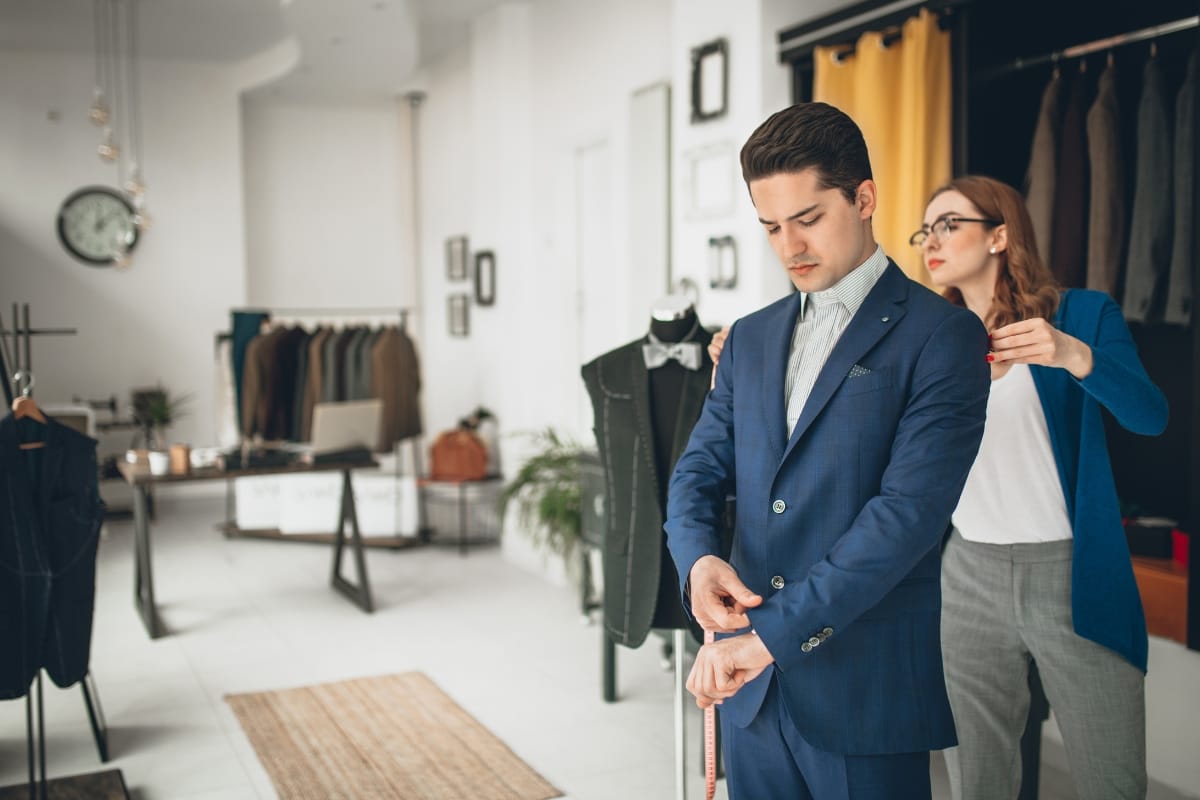 In a nod to a refined lifestyle, a tailor meticulously adjusts the sleeve of a man's blue suit in the upscale clothing store, ensuring every detail complements his sophisticated taste.