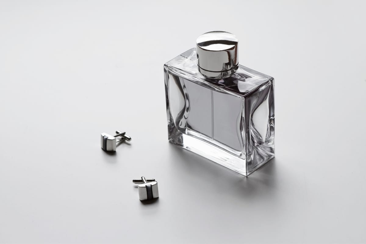 A bottle of cologne with a shiny, rectangular design sits on a surface next to a pair of silver cufflinks, embodying the sophisticated allure of a cigar lifestyle.