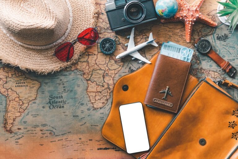 Flat lay of travel essentials: map, passport, smartphone, camera, globe, hat, sunglasses, compass, watch; perfect for exploring travel destinations for cigar lovers. Toy planes and a starfish add whimsical touches to your journey.