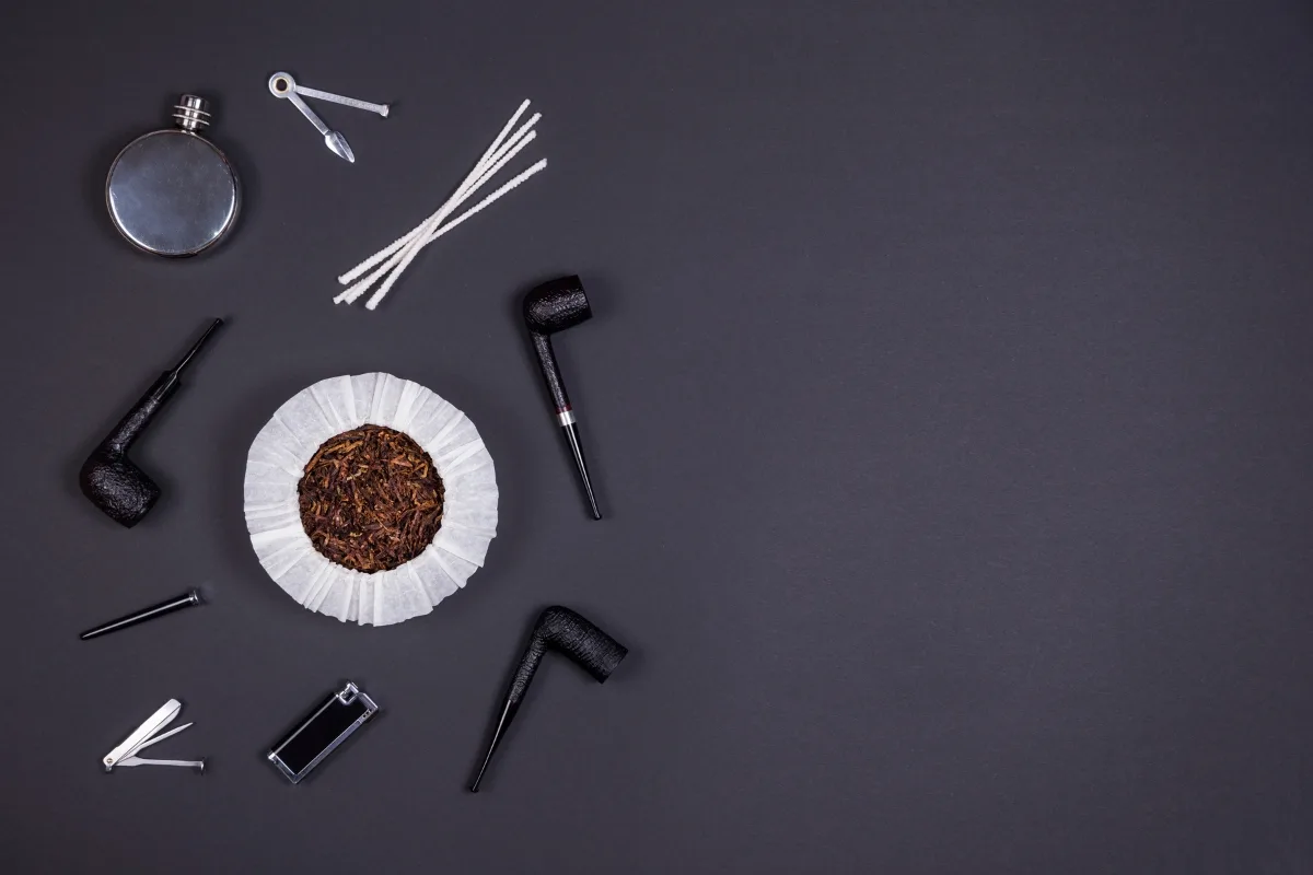 Smoking pipes, a tobacco pouch, cigarette holder, lighter, and essential smoking accessories are arranged on a dark gray background, highlighting the importance of tobacco pipe care.
