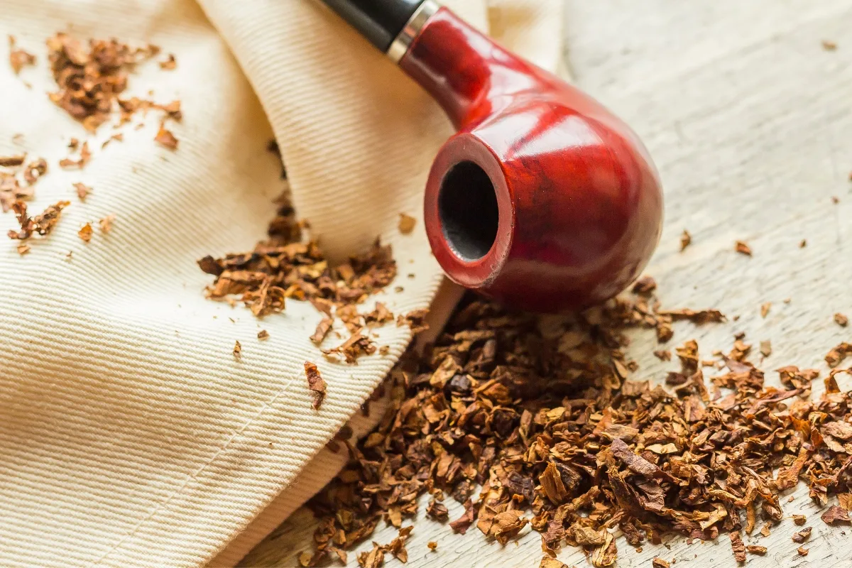 A red tobacco pipe and scattered loose tobacco rest on a textured fabric surface, exemplifying the essence of thoughtful tobacco pipe care.
