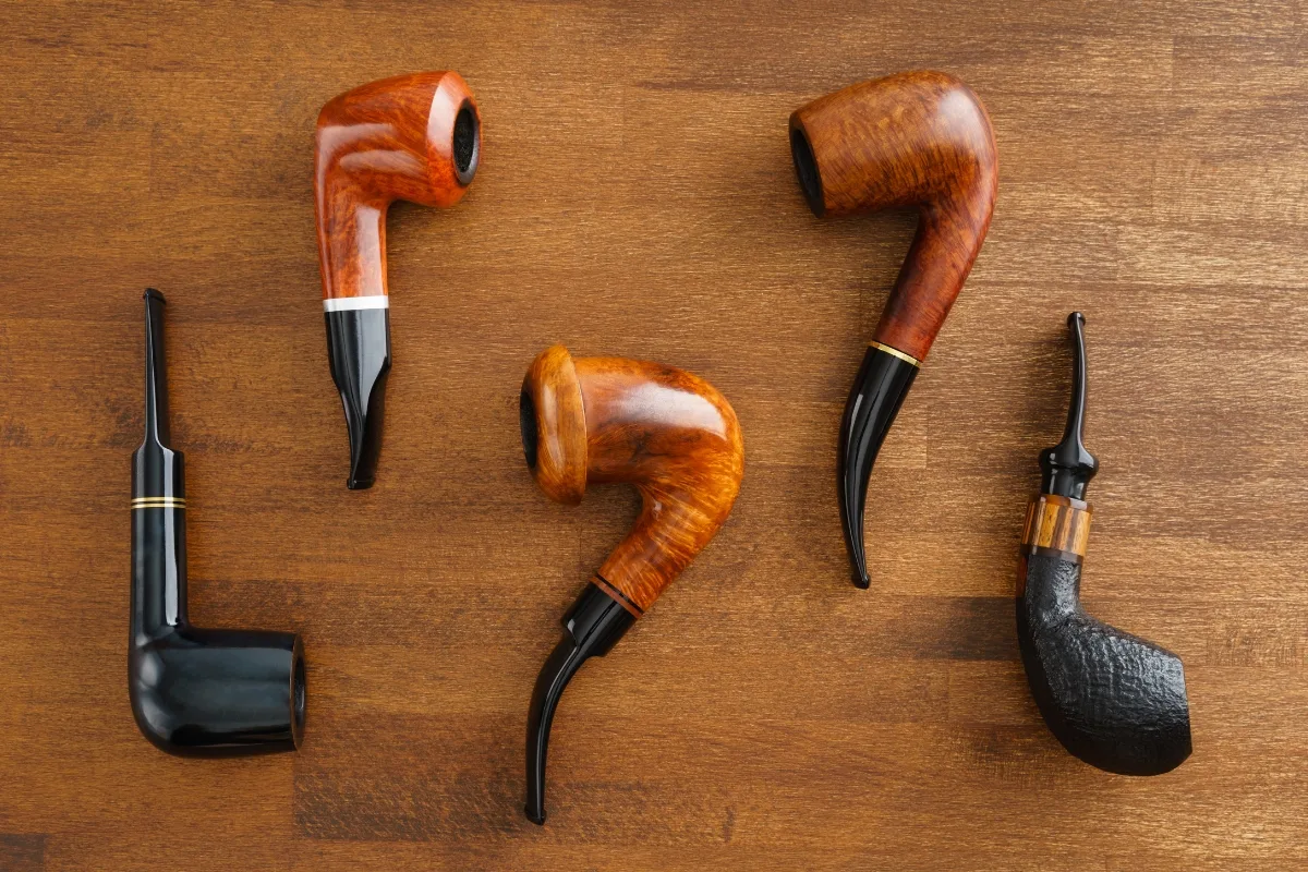 Five wooden tobacco pipes, showcasing a spectrum of shapes and finishes, are elegantly arranged on a wooden surface, inviting comparison to their rustic clay counterparts.
